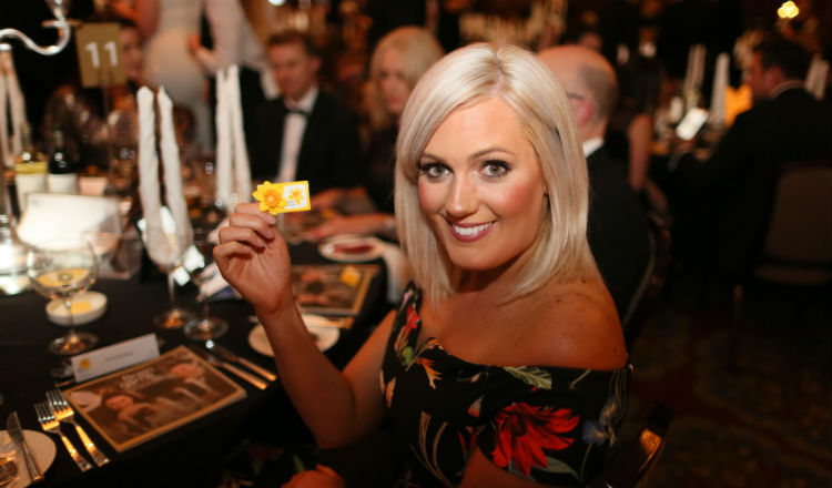 A Belfast Brain Game 2017 guest smiles as she holds up her Marie Curie daffodil badge