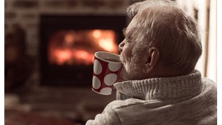 A man sits by a fire drinking a cup of tea
